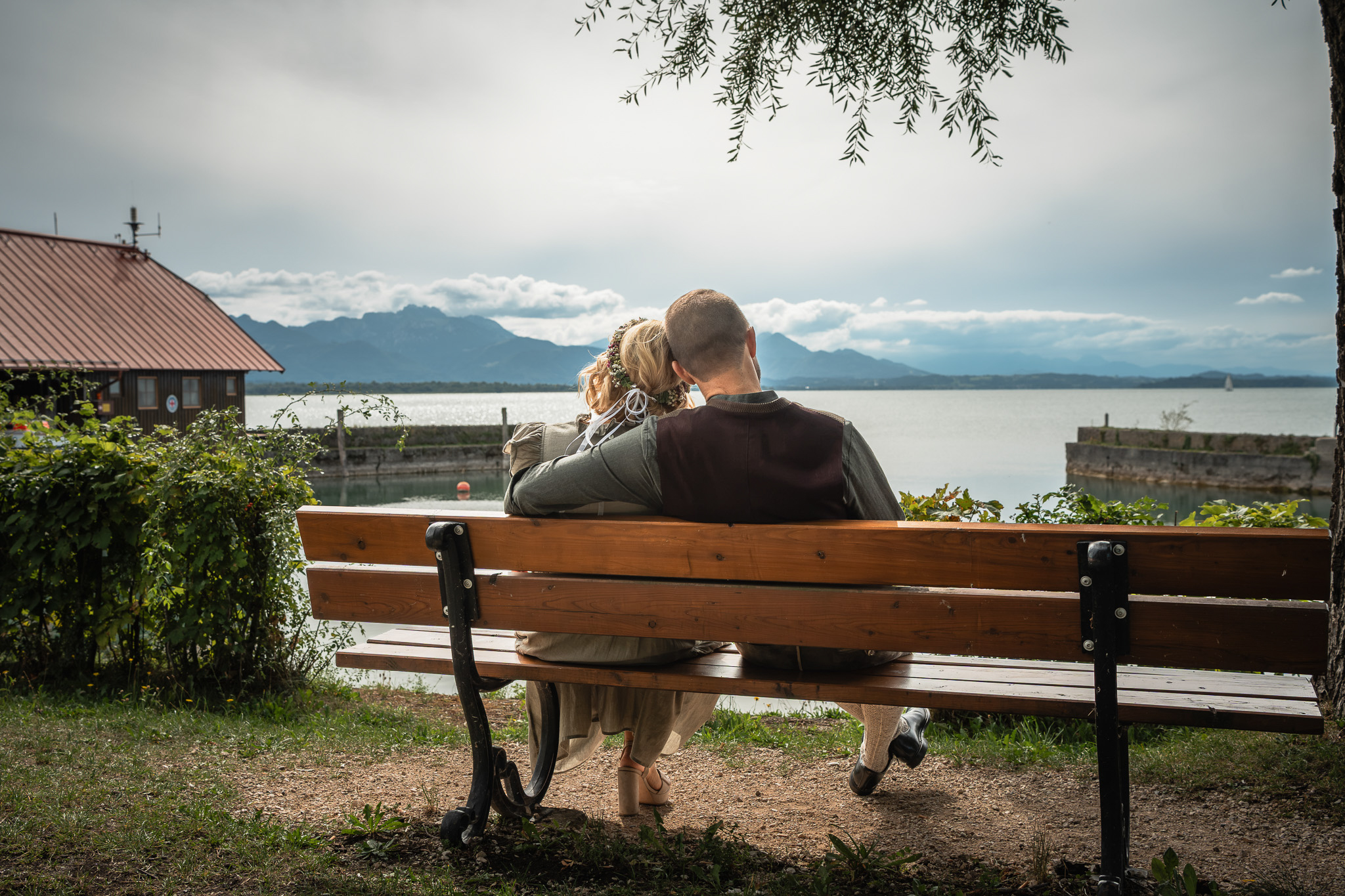Brautpaar sitzt auf einer Bank in Chieming und blickt über den Chiemsee auf die Chiemgauer Alpen