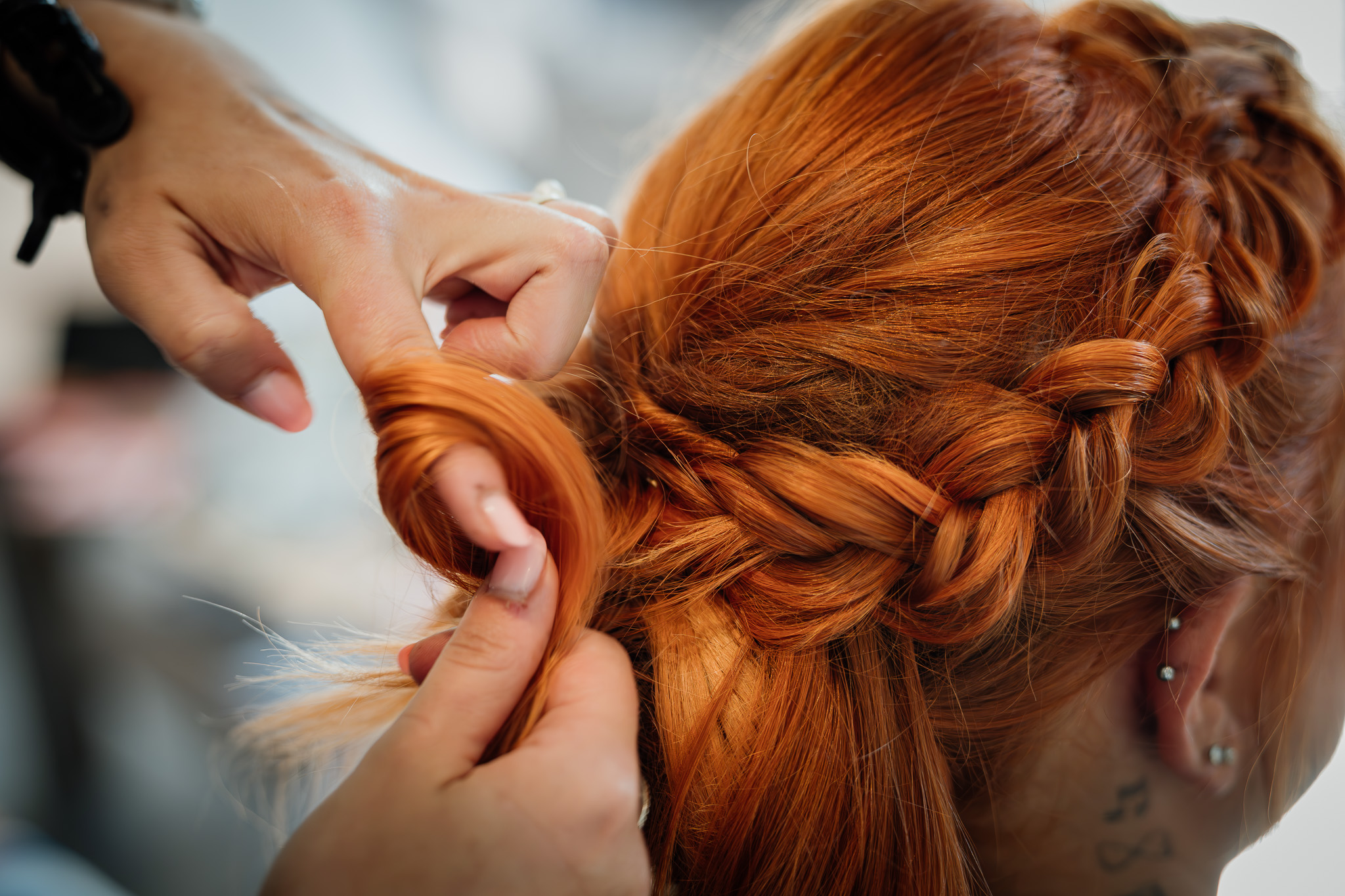 Die Stylistin formt Flechtelemente in die rote Brautfrisur.