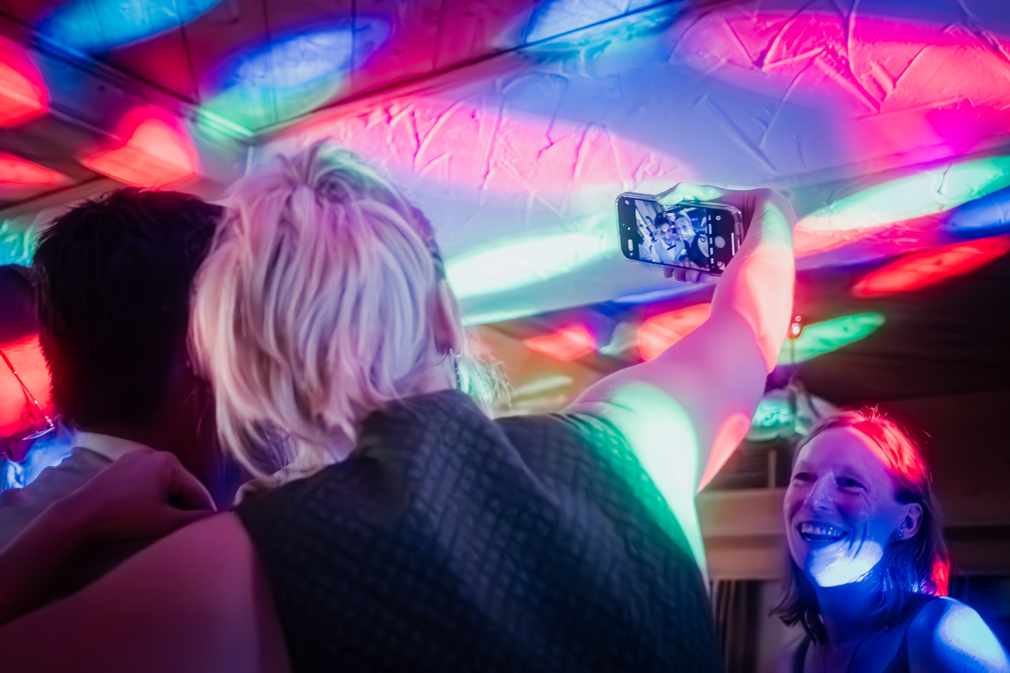 Hochzeitsgäste feiern unter buntem DJ-Licht ausgelassen miteinander.