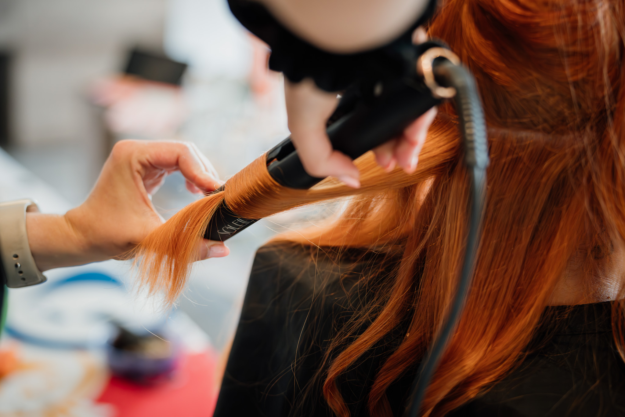 Die Stylistin arbeitet beim Getting Ready sorgfältig an den langen roten Haaren der Braut.