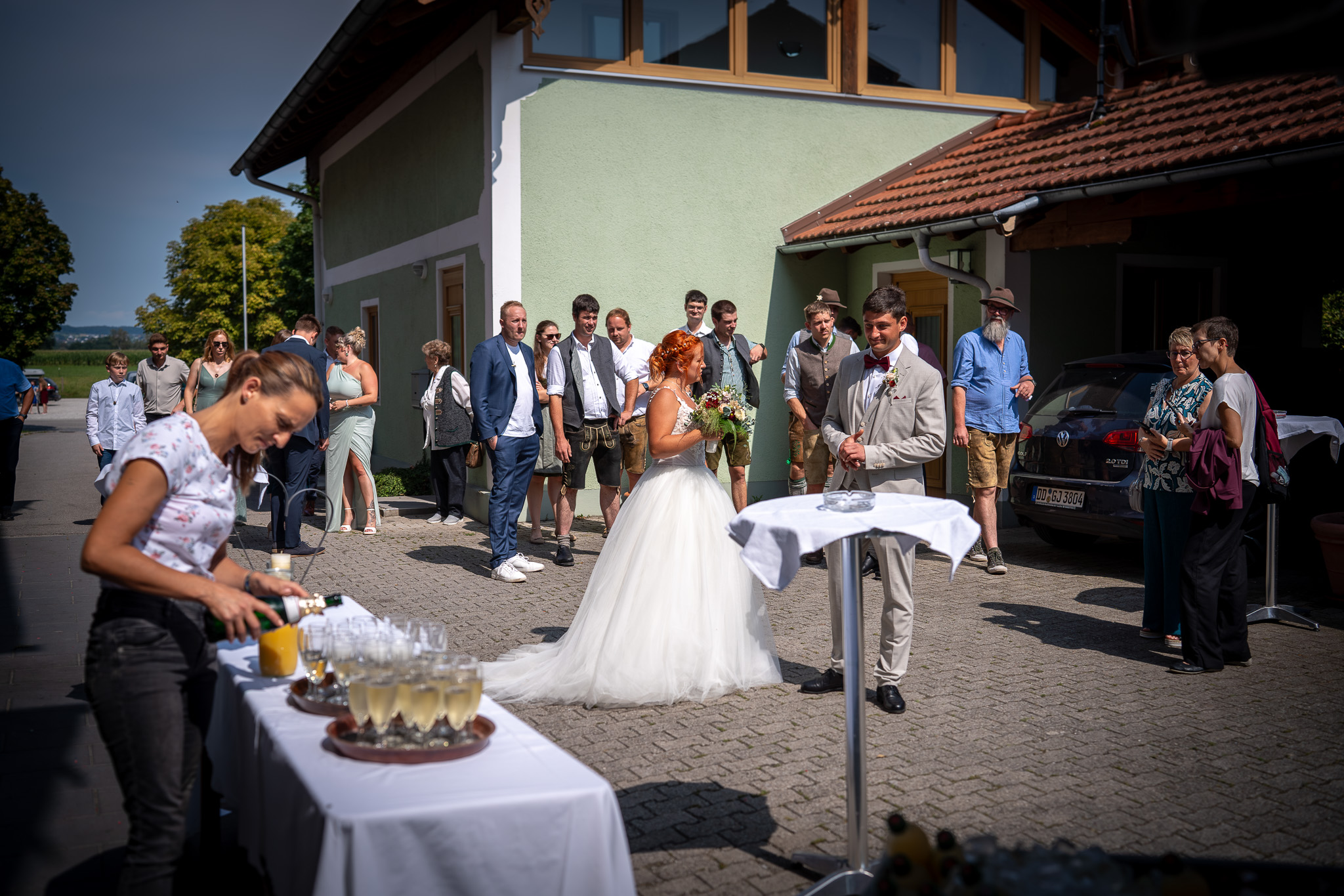 Brautpaar und Gäste treffen beim Sektempfang vor dem Wirt zusammen.