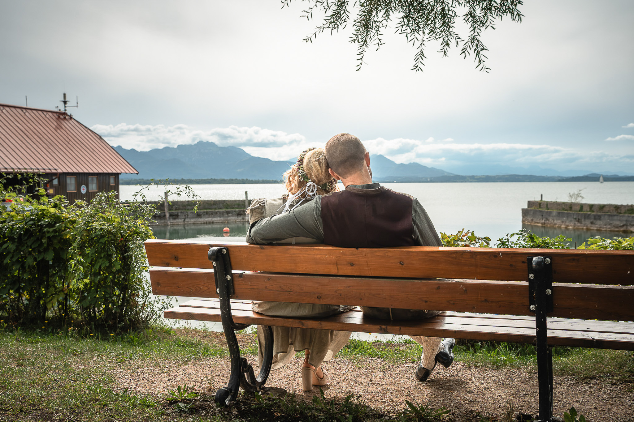 Brautpaar am Chiemsee mit Alpenpanorama | Lindl Photography Brautpaar sitzt auf einer Bank mit Blick über den Chiemsee und die Alpen.