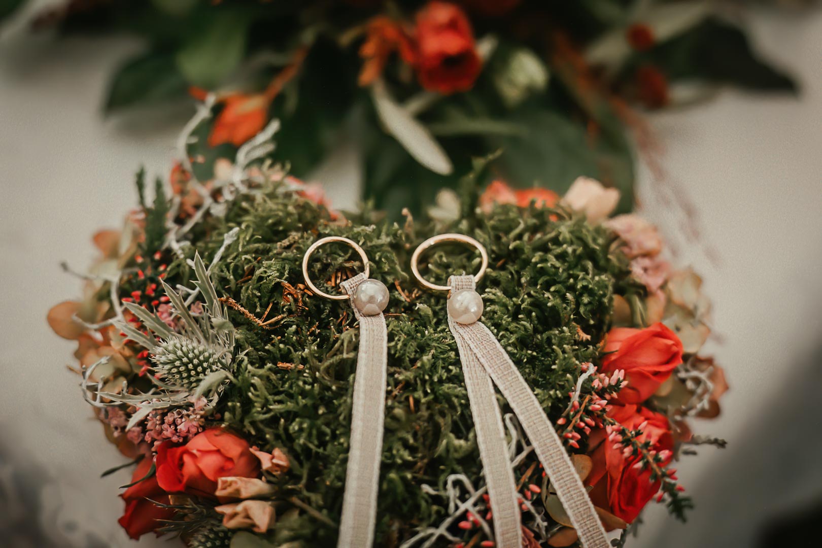 Eheringe und Hochzeitsdekoration – liebevolle Detailfotografie | Lindl Photography Zwei Eheringe liegen auf einem Blumenkranz mit roten Blüten.
