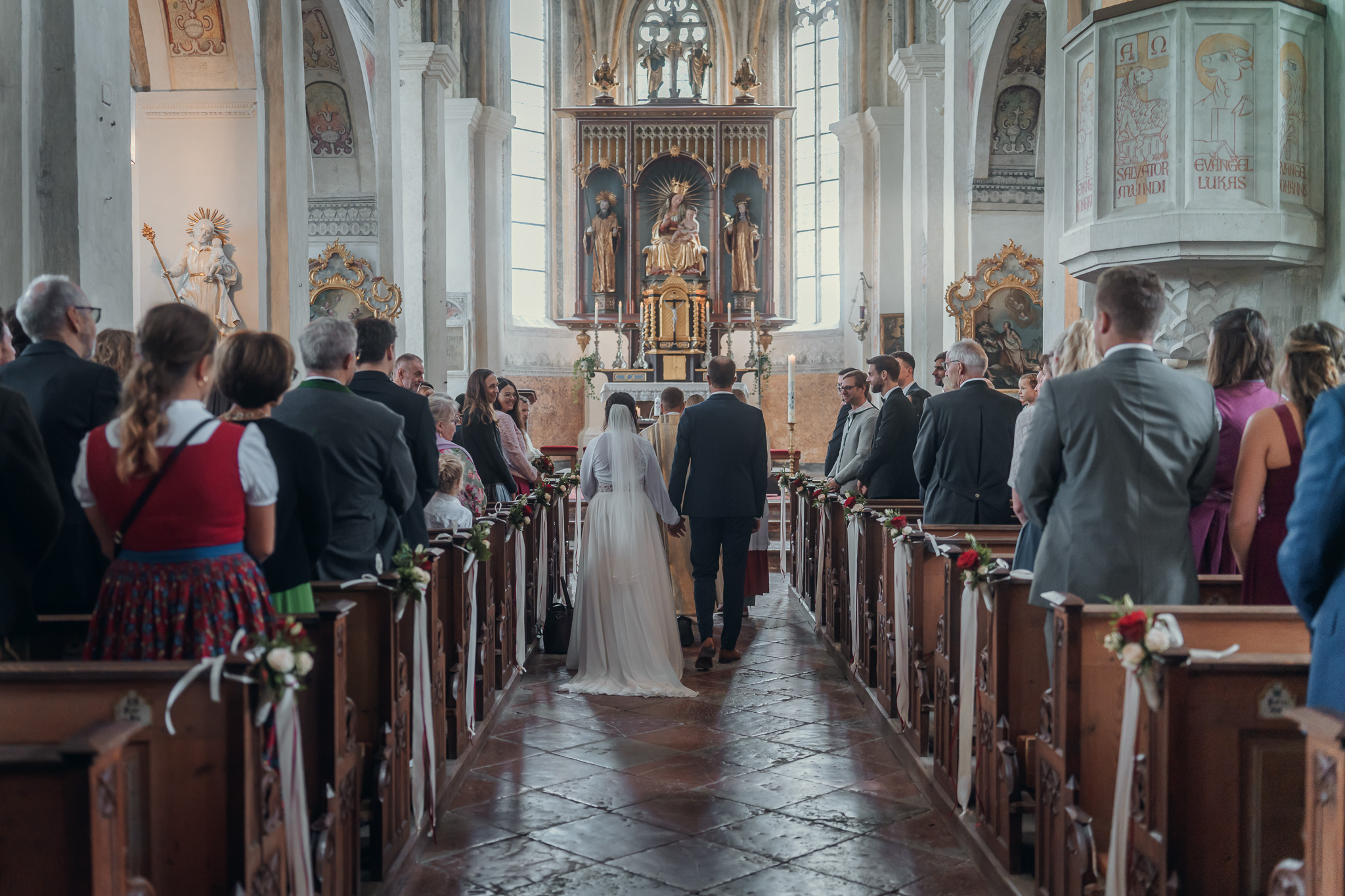 Brautpaar steht vorne in der Klosterkirche Seeon, die Hochzeitsgäste schauen zu.