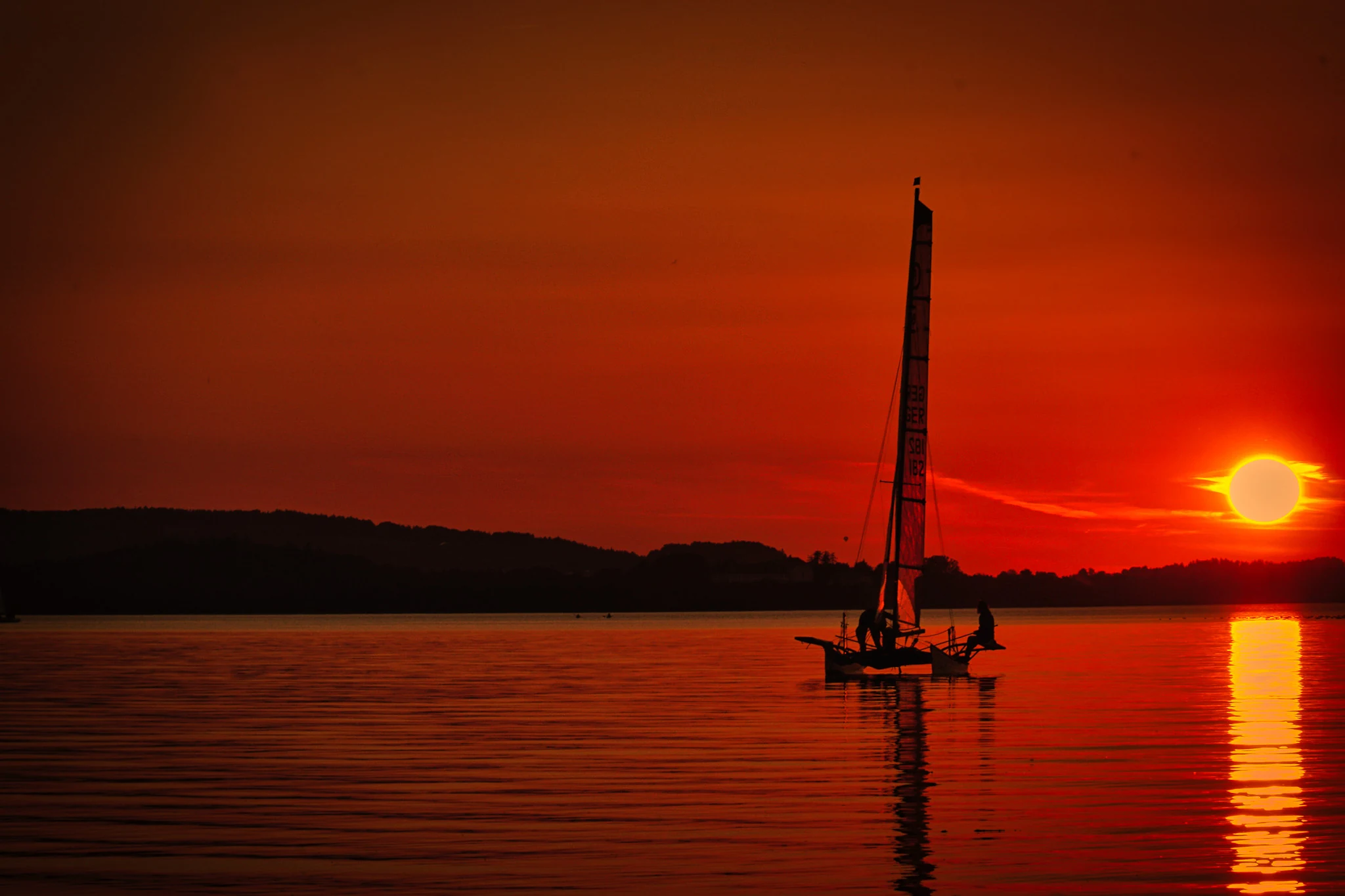 Segelboot vor der Beach Bar Übersee am Chiemsee bei intensivem Sonnenuntergang